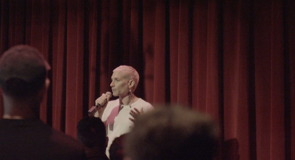 A performer speaking into a microphone on a theatre stage