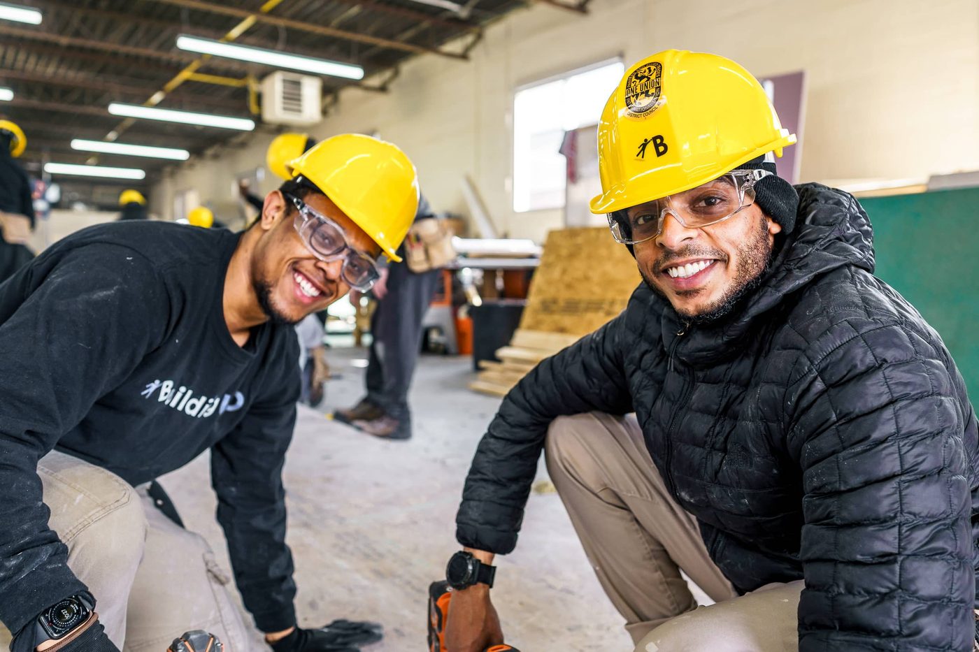Two trainees in hard hats and safety goggles in a construction workshop