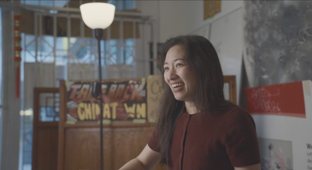A community organizer in front of a Take Back Chinatown poster