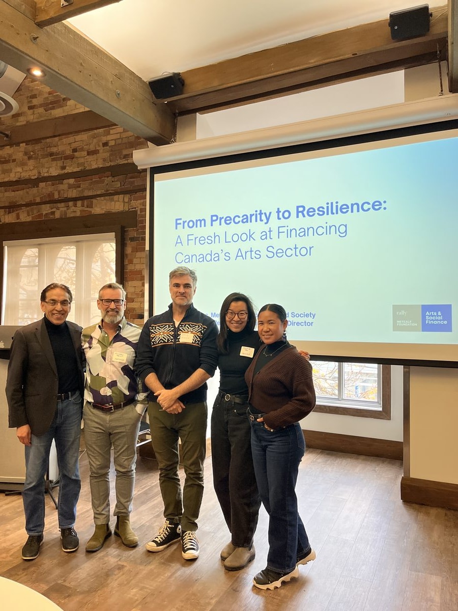 People standing in front of an Arts & Social Finance presentation slide